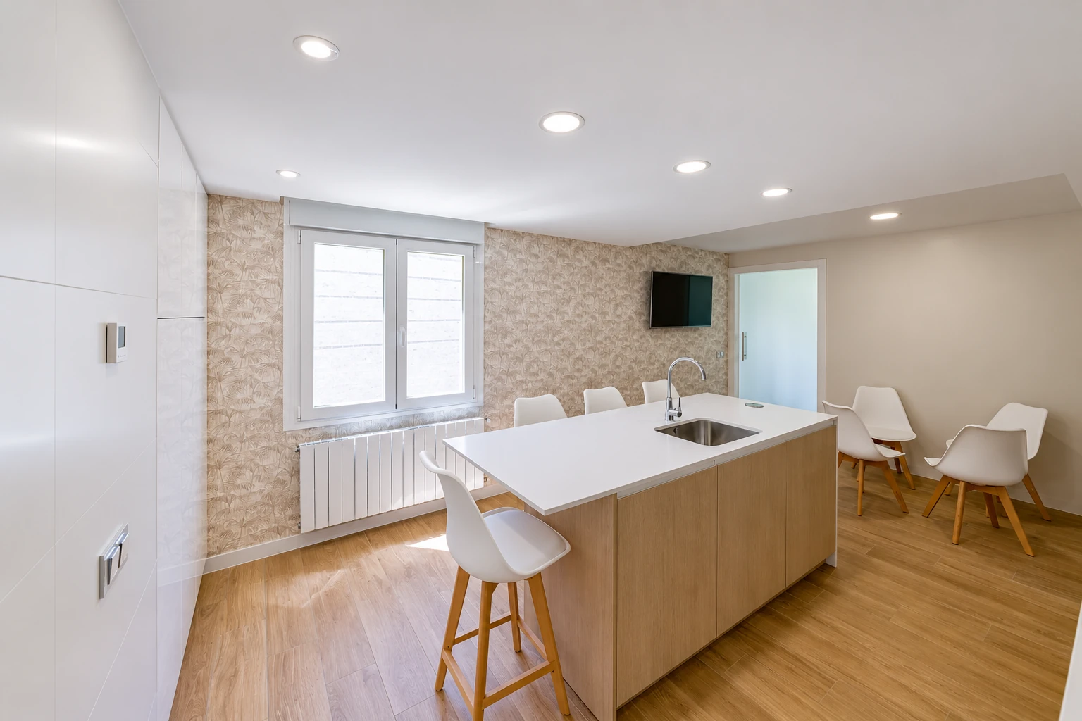 Cocina con isla blanca, madera y revestimiento vegetal en la vivienda del Barrio del Pilar.