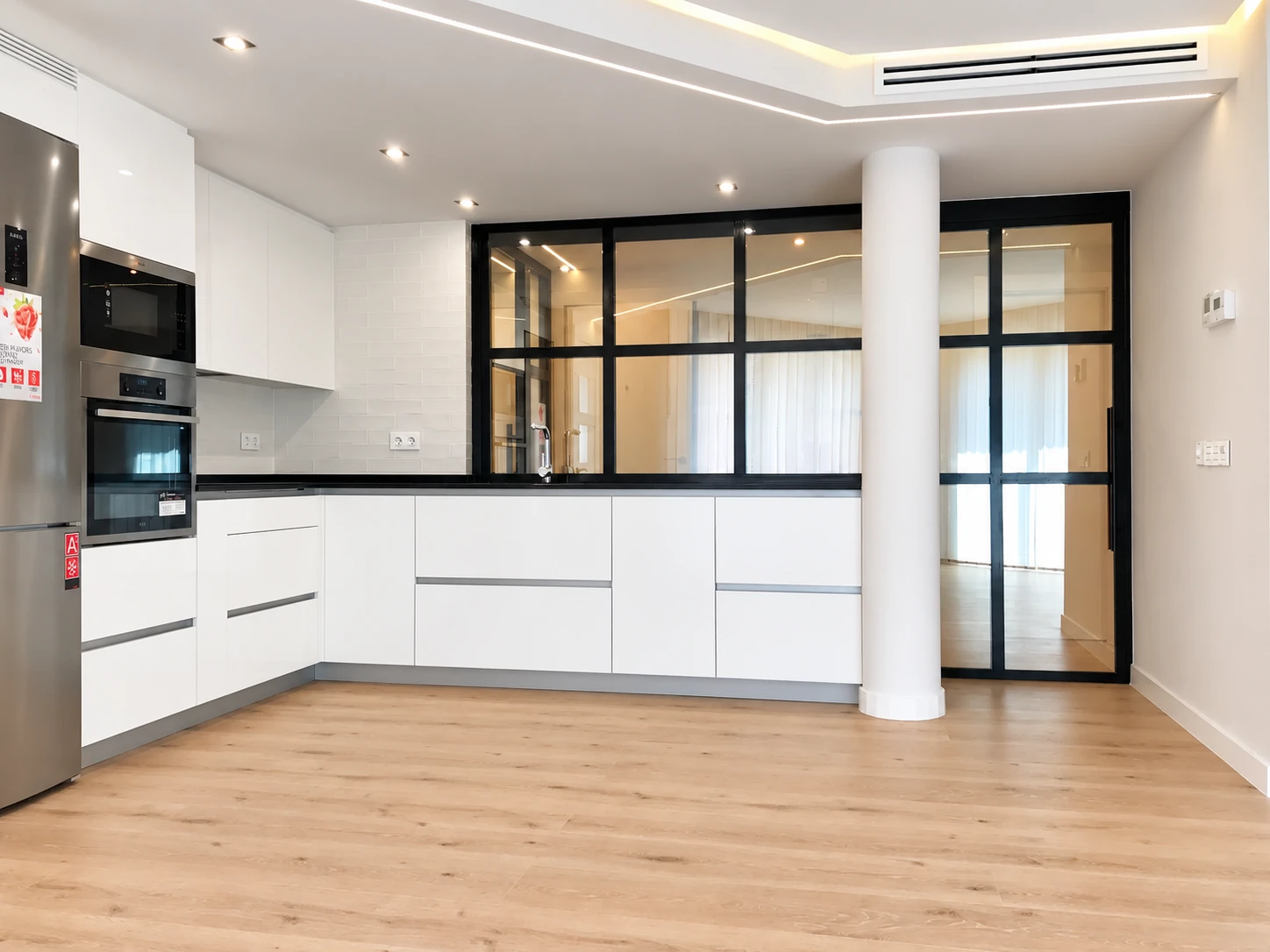 Cocina blanca abierta con cerramiento negro de cristal en la vivienda de División Azul.