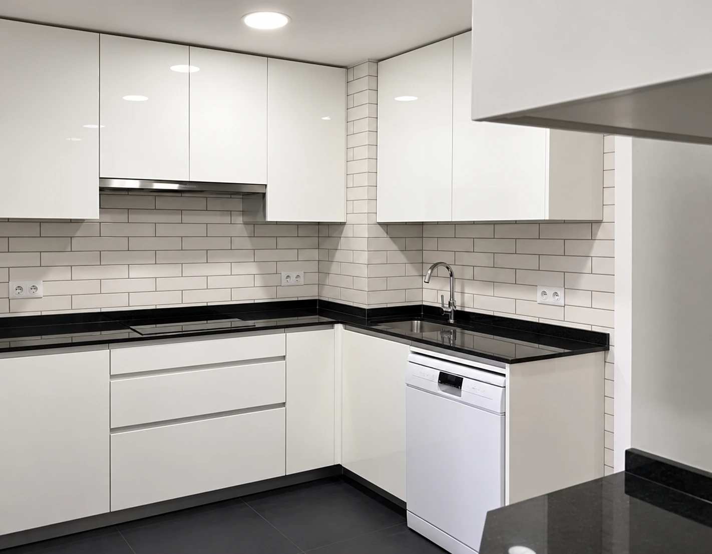 Cocina blanca con encimera negra y azulejos blancos en la vivienda de Juan Sánchez.