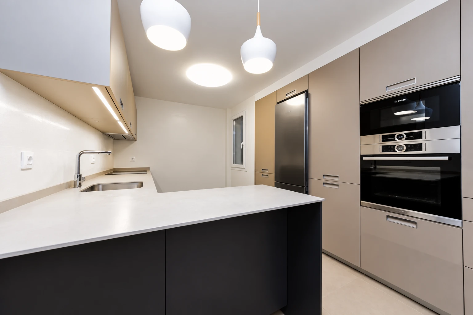 Cocina con península, muebles en tonos neutros y electrodomésticos integrados en calle Zafra.